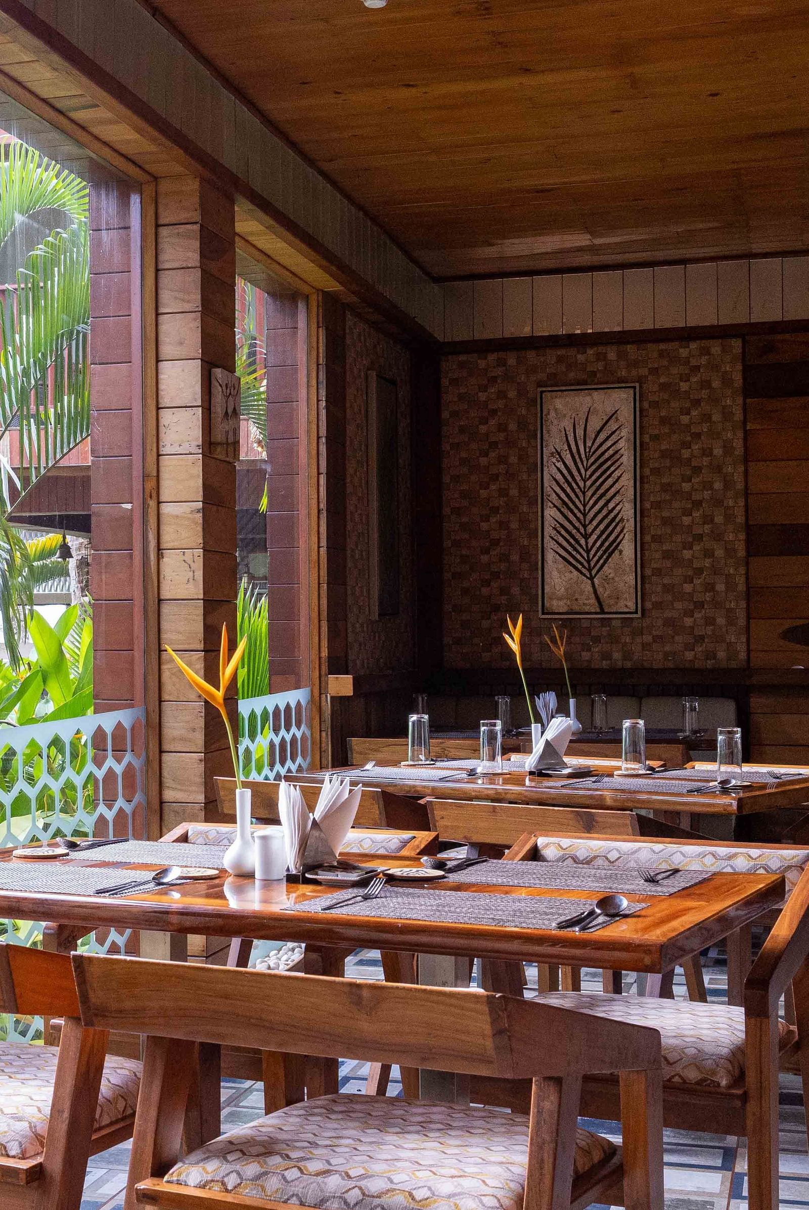 A restaurant with wooden furniture, with a balcony view to the lush greenery outside.