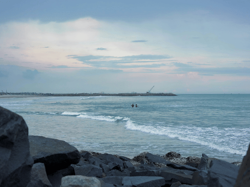 Gentle waves roll towards the rocky shoreline beneath soft afternoon light by sea