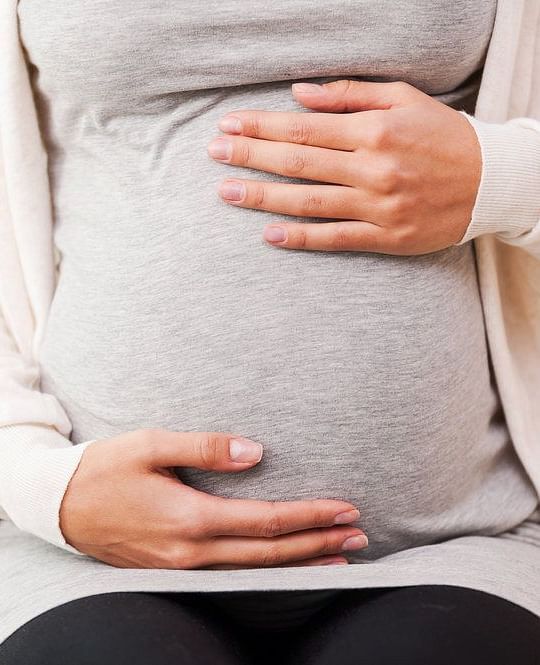 A woman dressed in grey t shirt holding her baby bump - Brewery Gulch Inn & Spa