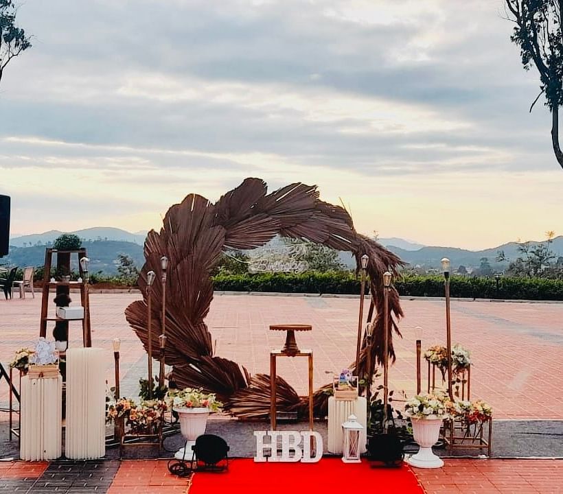 An outdoor wedding venue is set up with a floral arch and red carpet, with a scenic view in the background | Open Deck | Woodstock Resorts, Coorg