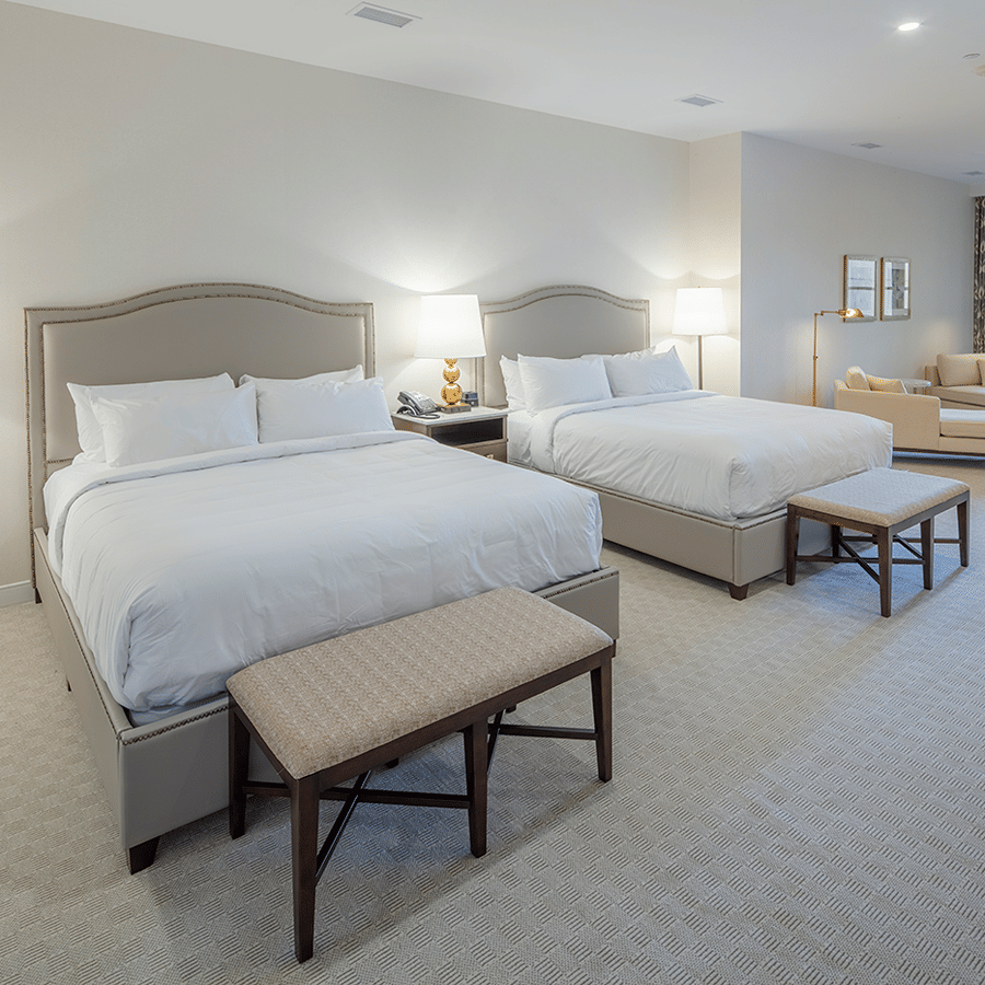 A spacious guest room with two large beds, bedside lamps, upholstered benches and a seating area by the balcony doors at YO1 Longevity & Health Resorts, Catskills