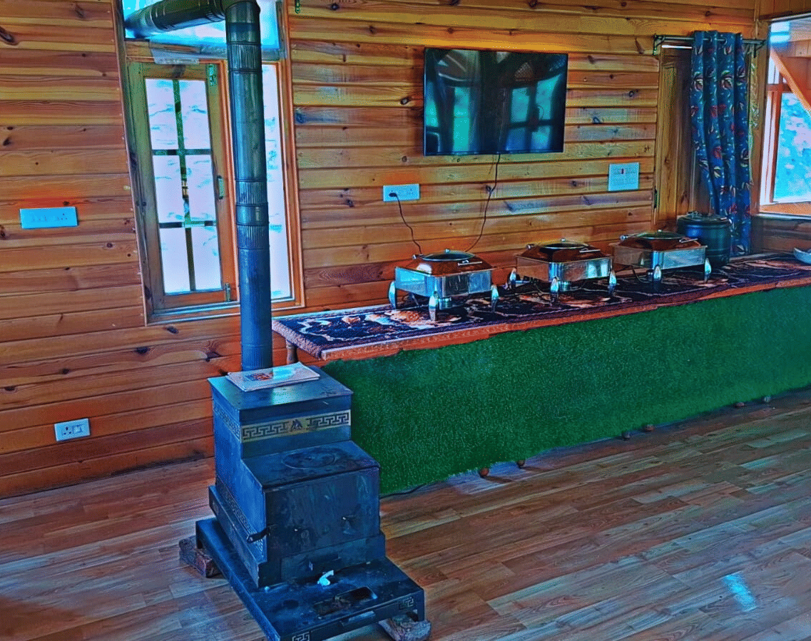 An indoor buffet counter at Dawat e Drung by FrozenFall Resort, Drung, Tangmarg, with dishes arranged on a long table in a wood-panelled room.