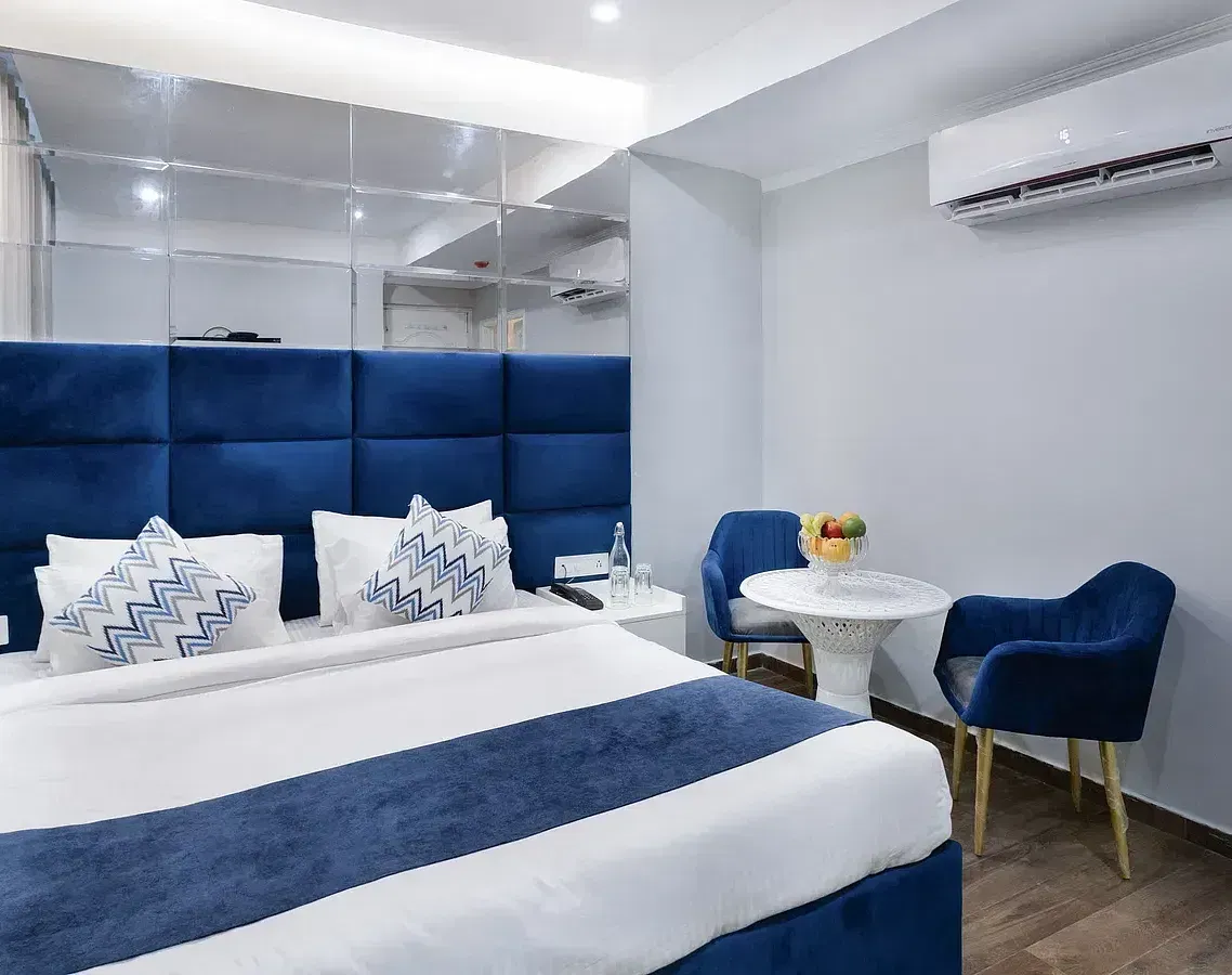 Deluxe Room featuring a king size bed with blue accents, a small table with two chairs, and minimalist decor. - Hotel Downtown17, Chandigarh