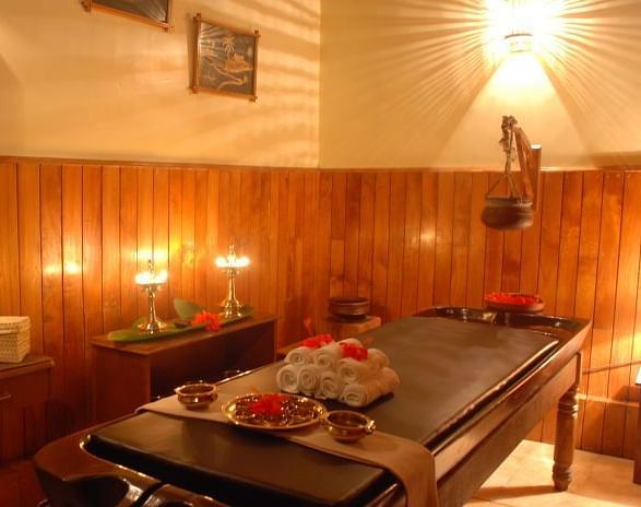 Warmly lit spa treatment room with a massage table and various wellness products - BluSalzz Collection - Tranquil Resort, Wayanad