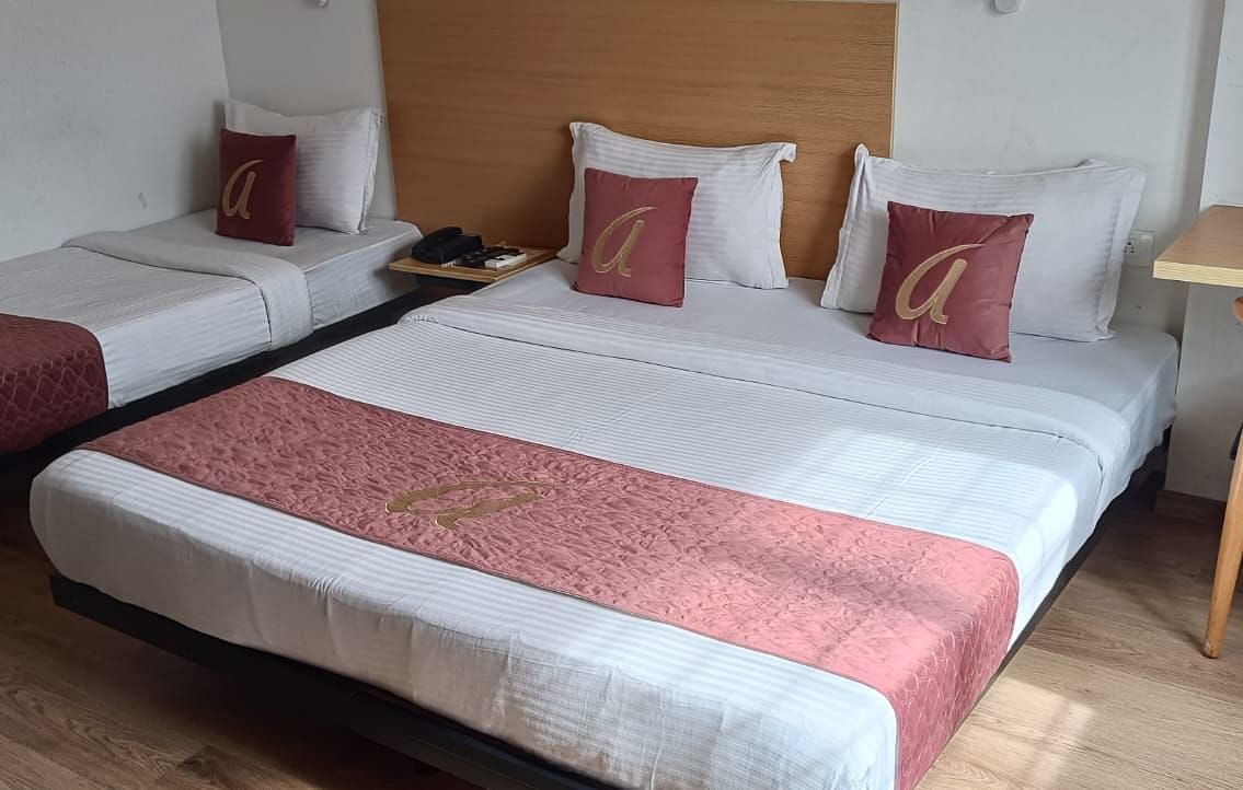 A well lit  bedroom with two beds, red cushions and a table  at Astra Hotels and suits, Sarjapura.