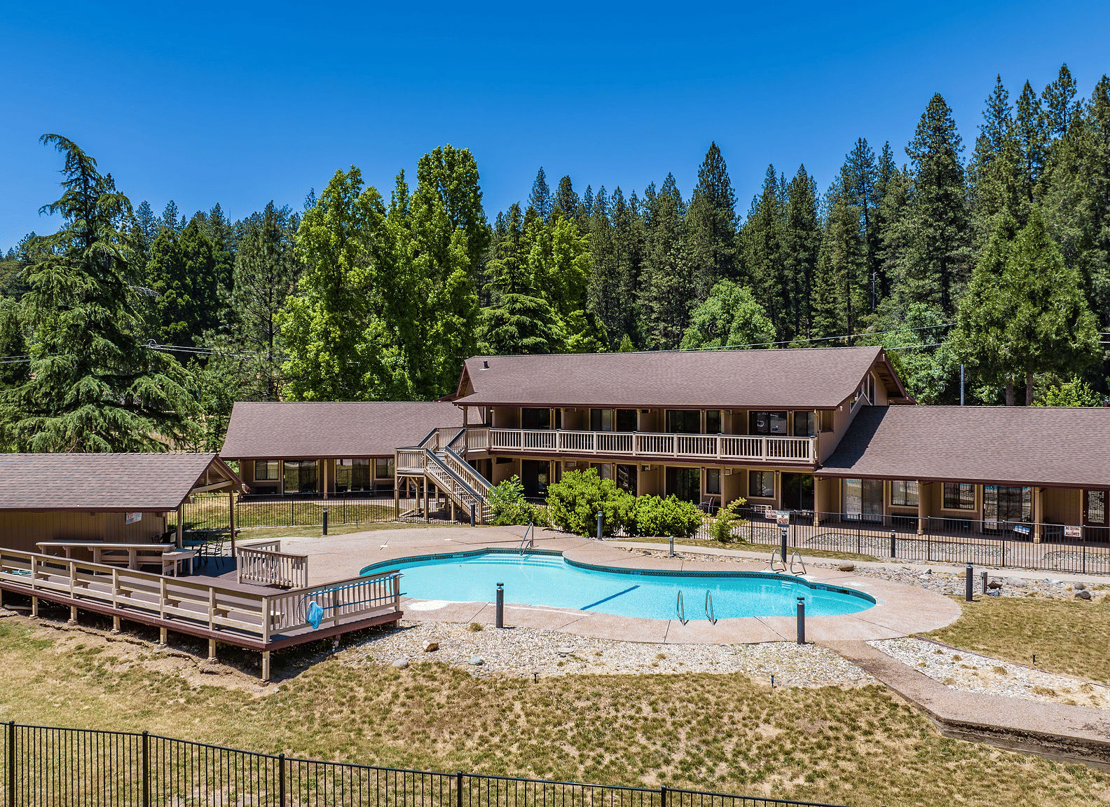 An aerial or elevated view of a multistory hotel complex nestled in a forest, featuring an outdoor swimming pool and sun deck - Amador Hotel