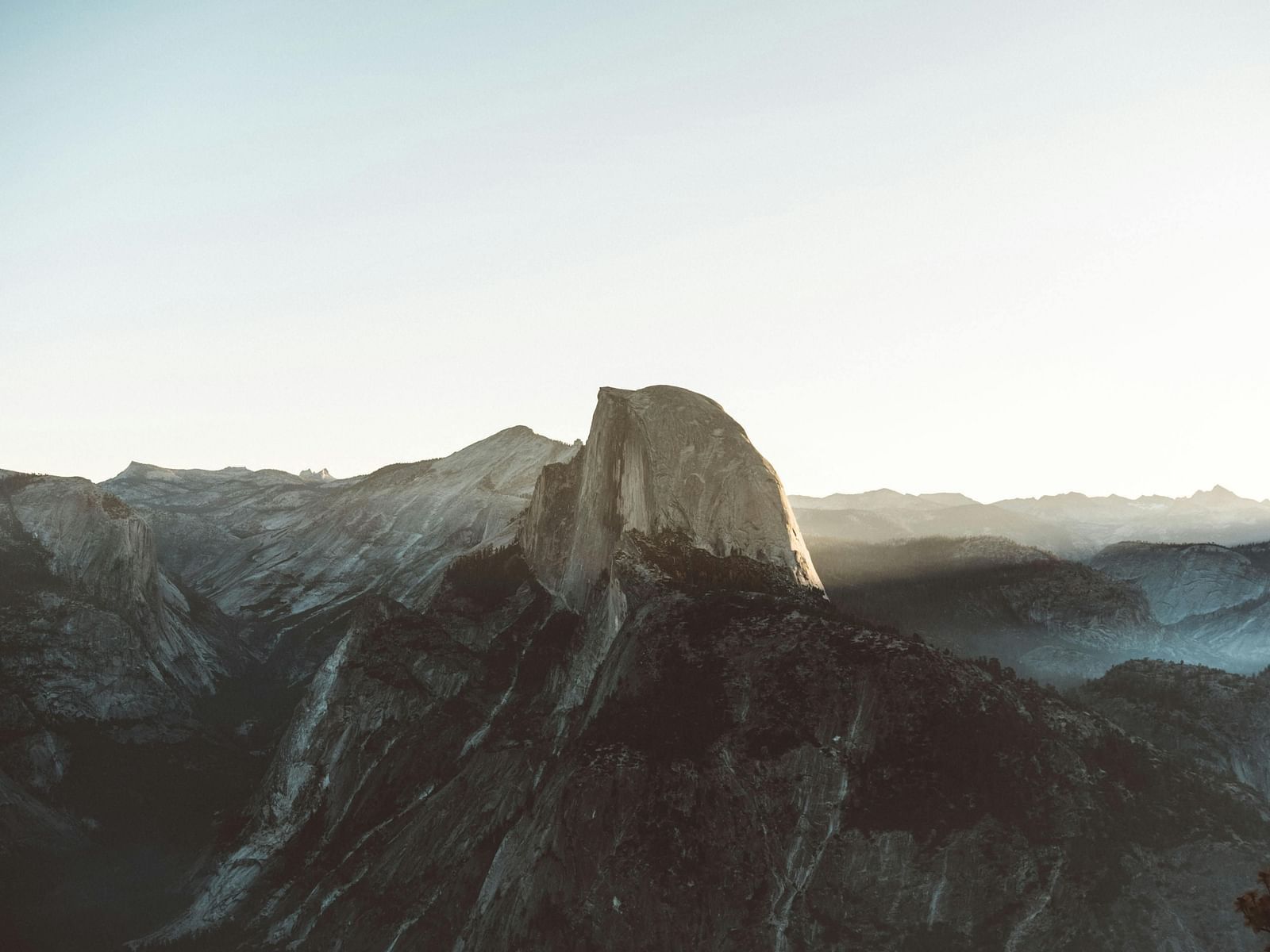 A breathtaking view of Glacier Point in Yosemite with a towering peak bathed in soft, golden sunlight, surrounded by rugged mountain ranges.