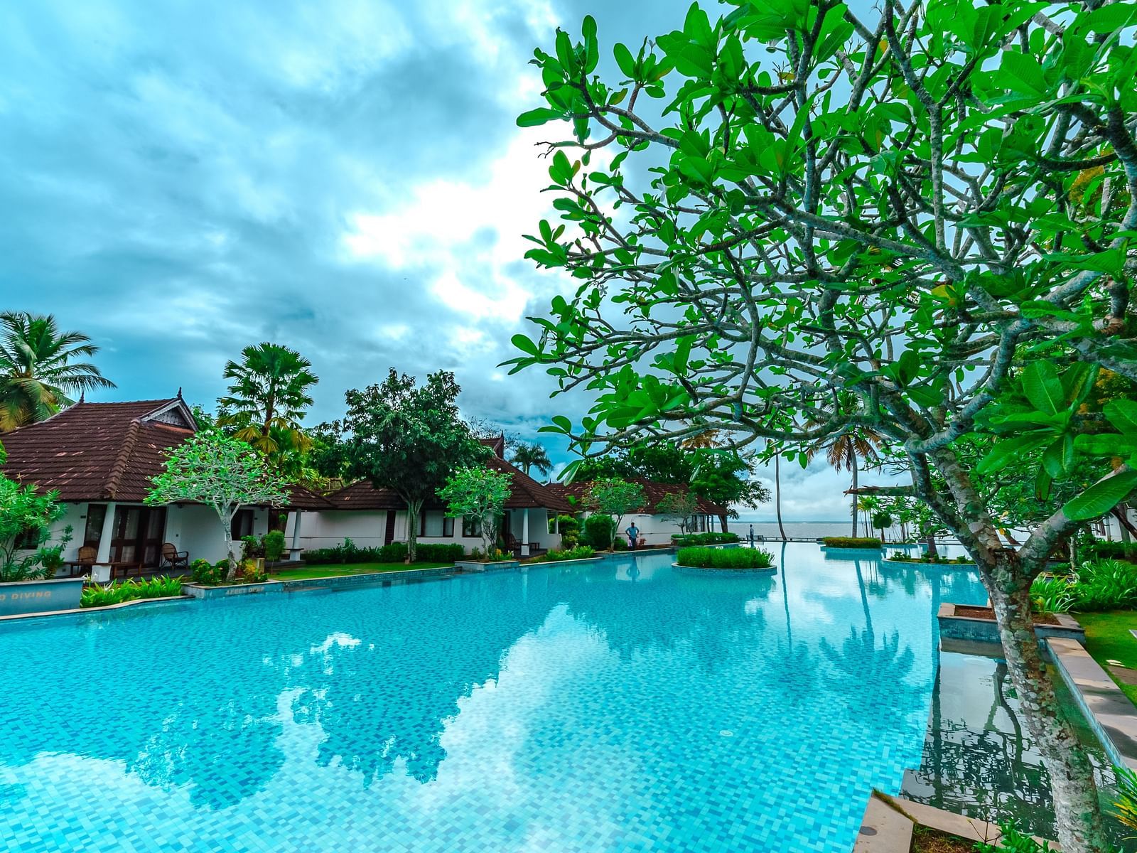an image of a swimming pool with rooms and trees in the entrance - Rhythm Kumarakom