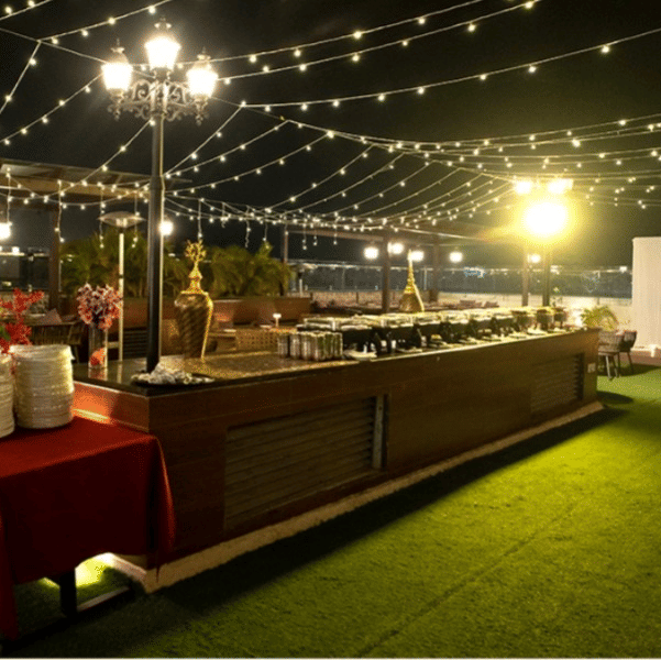 Night view of an outdoor banquet setup at Five Elements Hotel with fairy lights, a buffet counter, green lawn, and warm ambient lighting.