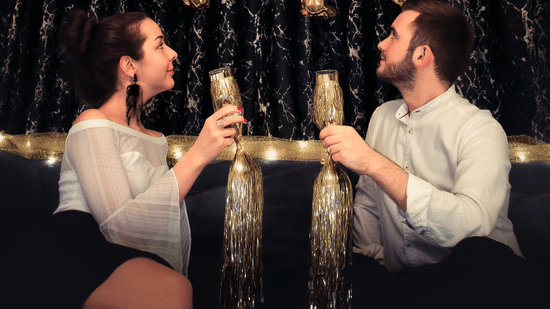 A couple holding drinks with happy new year made out of ballons on the wall