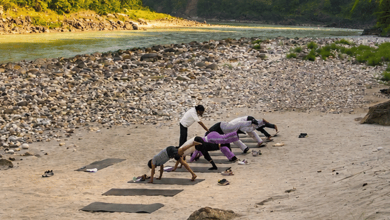 A group of people indulging into an early morning yoga session by the Ganges, with a beautiful backdrop of the hills.