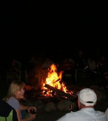 A campfire event at Kit Carson Lodge & Restaurant shows two people sitting near a fire at night. 