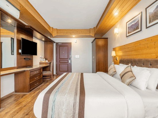 The suite room at Voyage Alpine Abode, featuring a double bed with linens and a striped runner, wooden wall panelling, a television, a built-in dressing table and framed  wall arts.