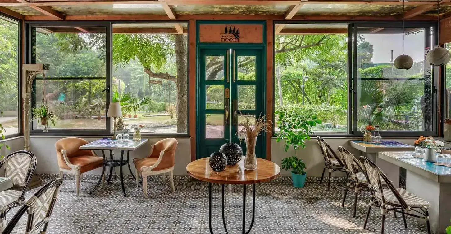 Glass-enclosed café-style seating area with garden views at Karma Chalets | Best Pet-friendly resort near Delhi