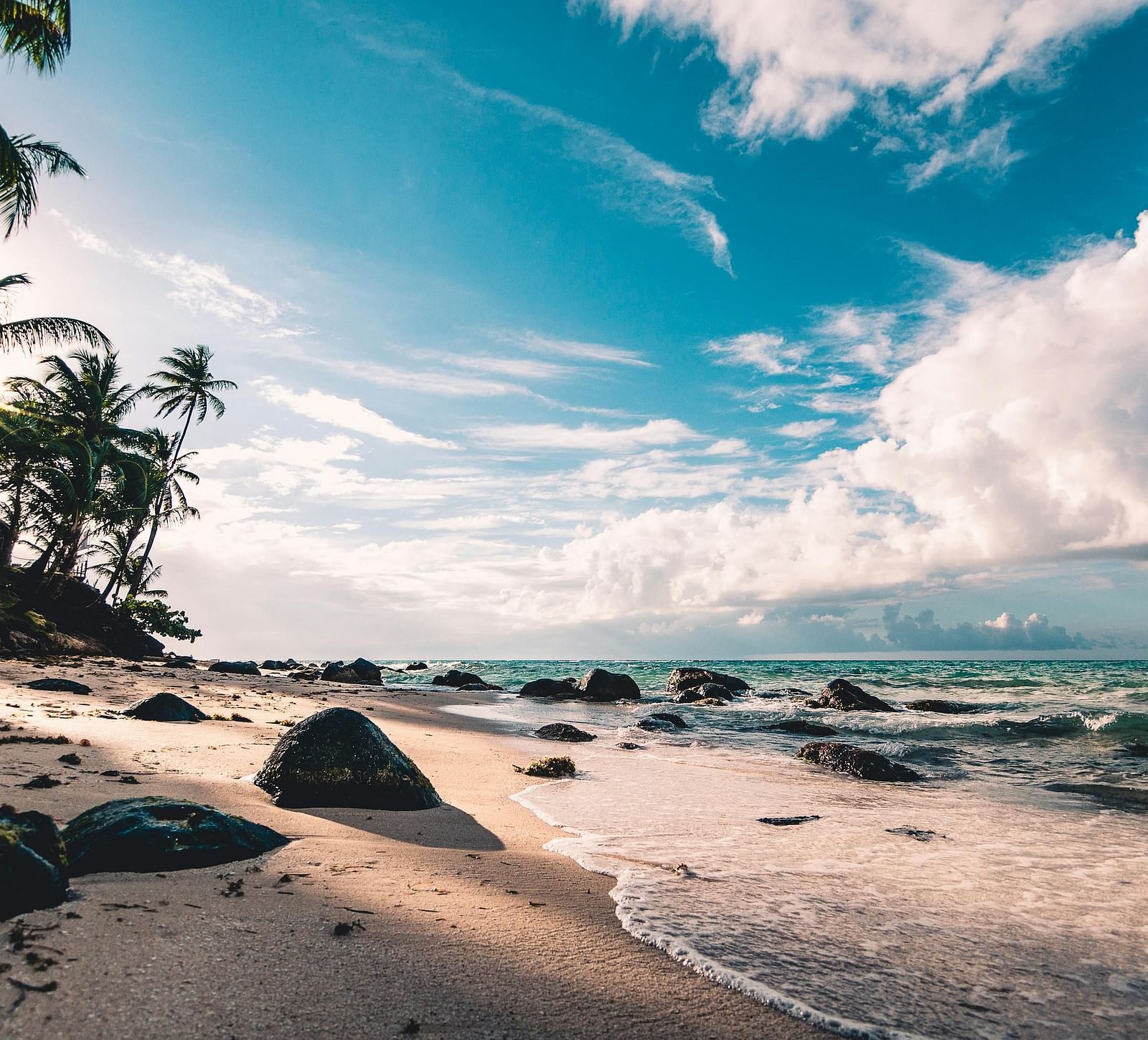 Beach view showcases gentle waves lapping at the shore, framed by rocks and trees under a partly cloudy sky