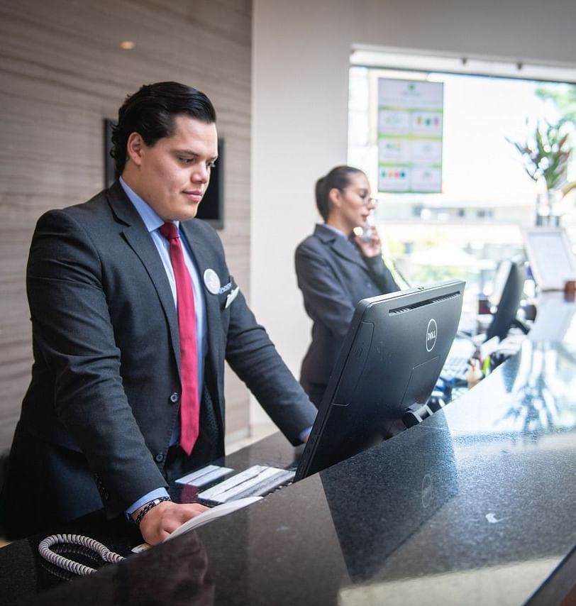 2 staff members standing behind the reception desk looking at the computer in front of them.