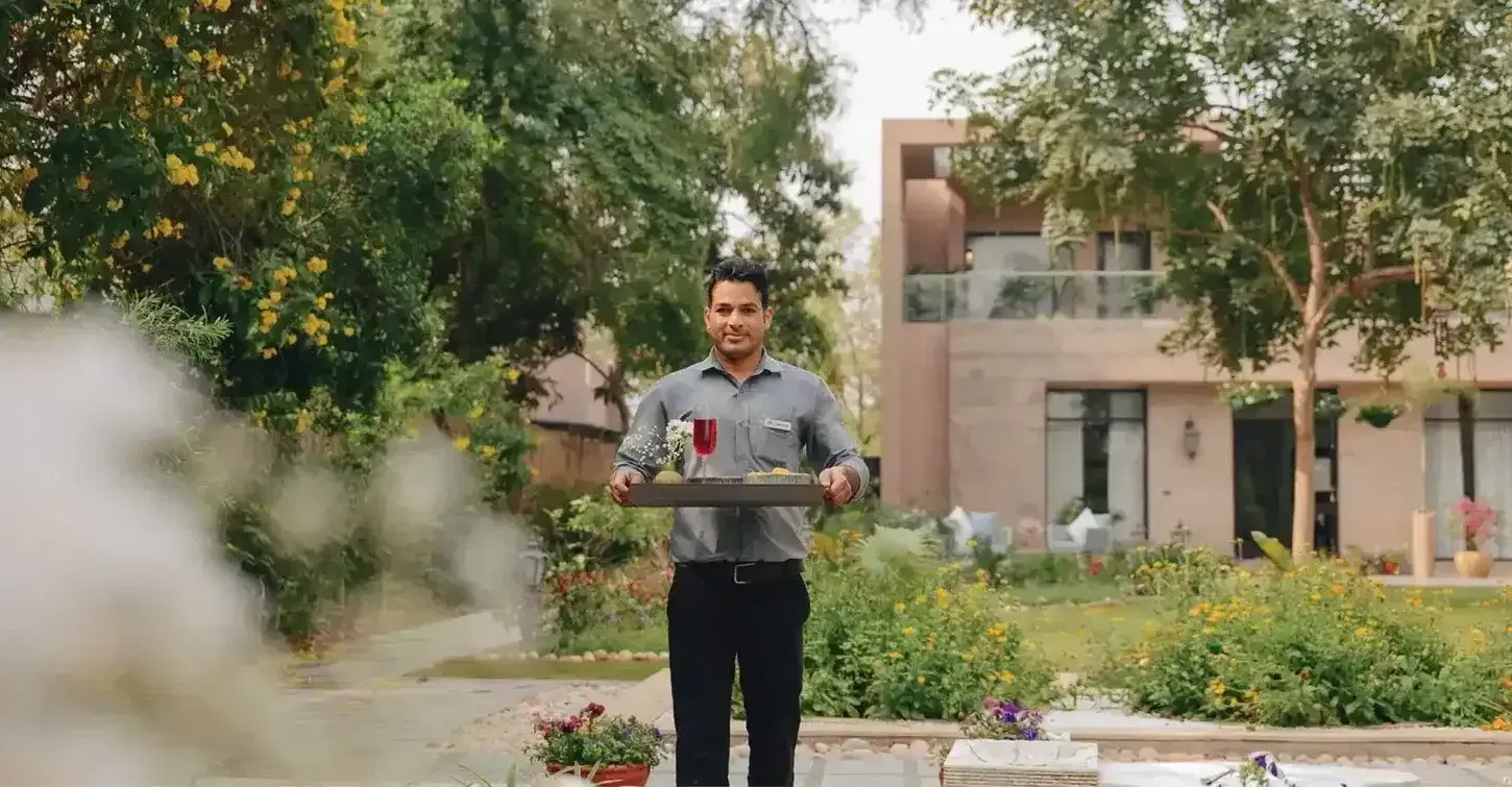 A waiter at Karma Chalets, our luxury hotel in Delhi NCR,  holding a tray of food with a building behind.