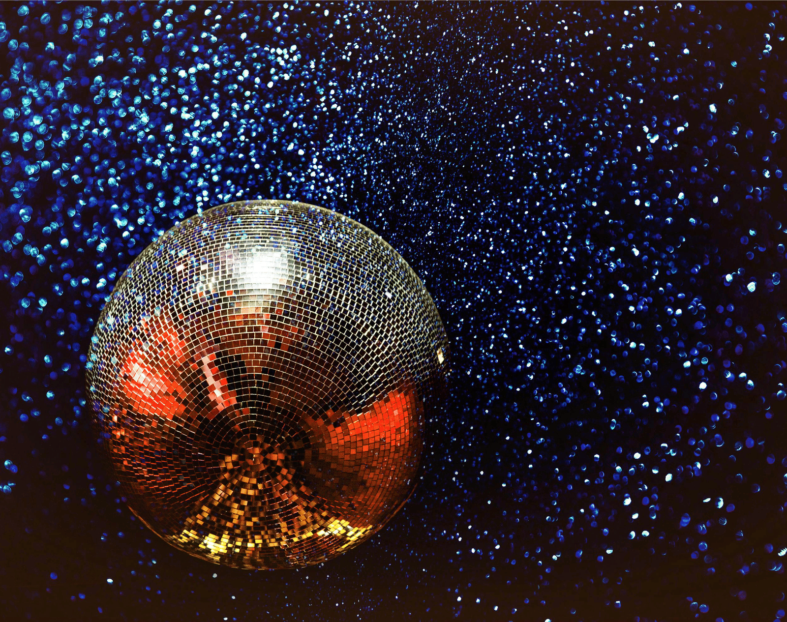 Shimmering disco ball reflecting colourful lights against a dark sparkling background.