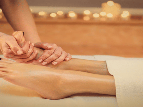 A couple of hands is giving a foot and lower leg massage to a person lying on a table