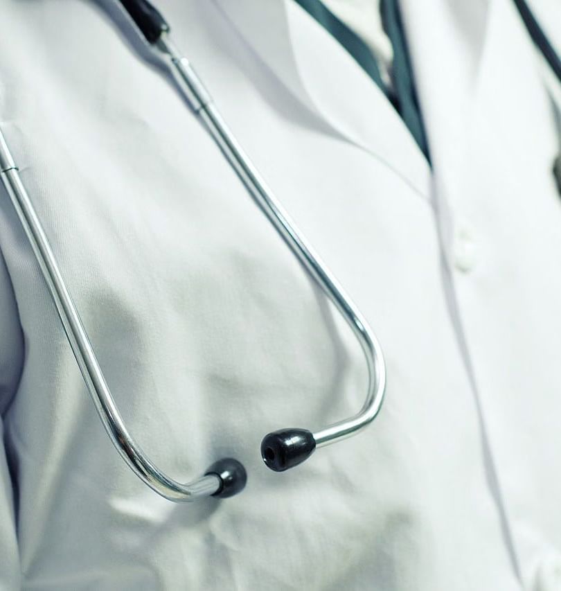 A close-up of a stethoscope hanging around the neck of a doctor wearing a white coat.