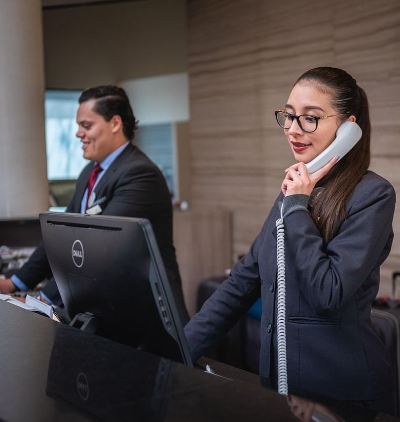 2 staff members standing behind the reception desk with desktops in front of them.