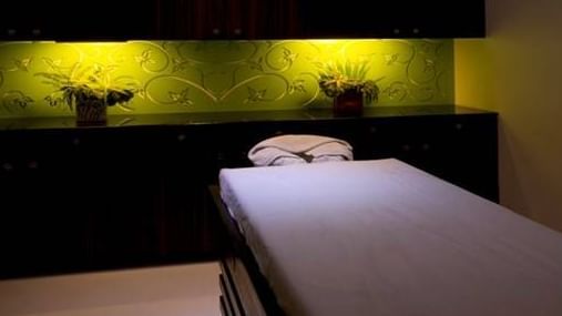 A massage bed at Springs Hotel & Spa, Bangalore in a dimly lit spa room with dark wood cabinets and a decorative green wall panel with potted plants