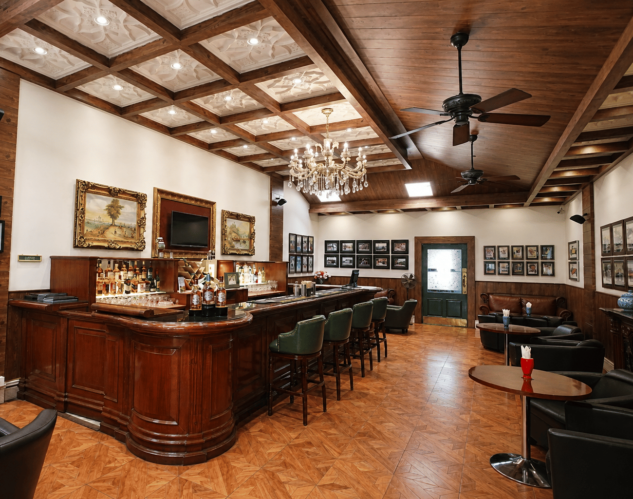 John's Tavern bar with a polished wooden counter, green leather stools, a crystal chandelier and framed vintage prints at MAYFAIR Himalayan Spa Resort, Kalimpong.