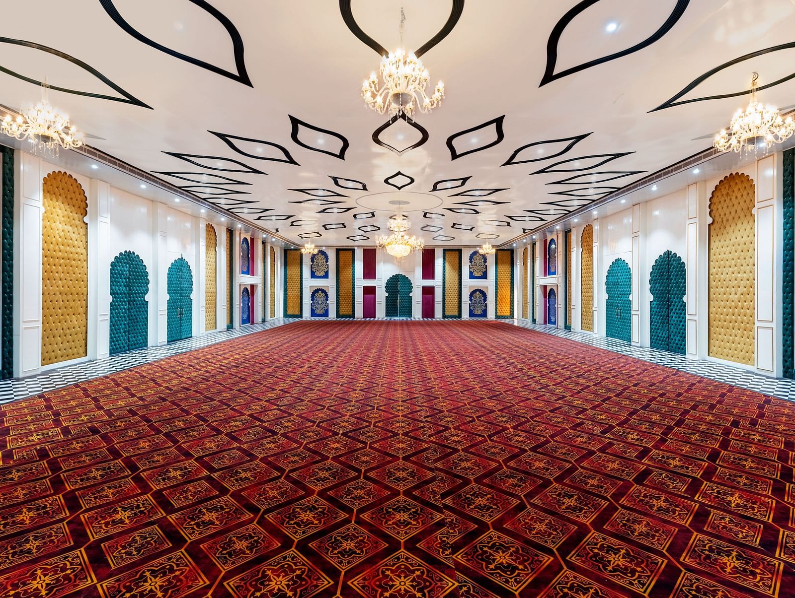Grand event hall with red patterned carpet, arched doorways, ornate ceiling lights, and golden-accented interior decor.