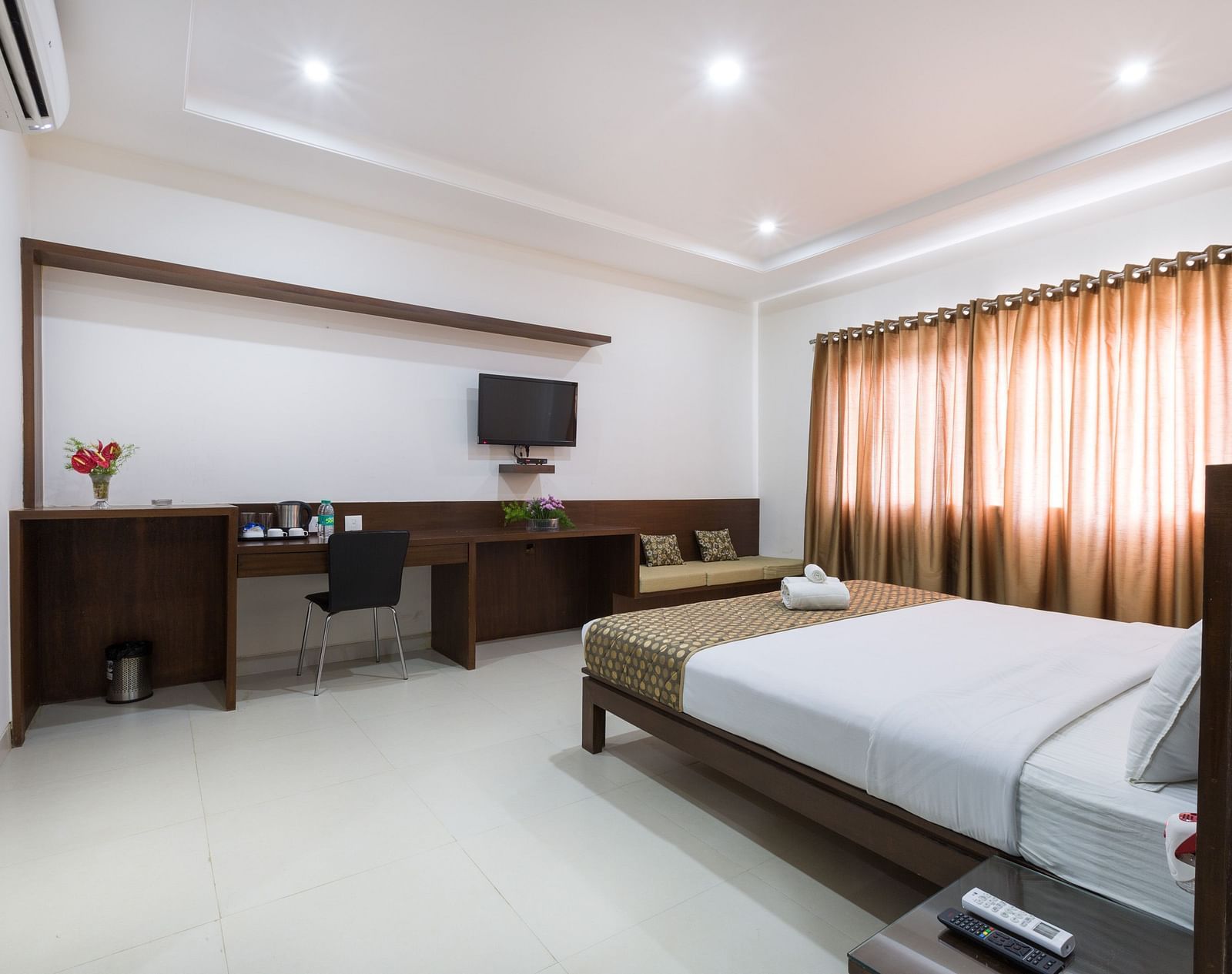 A well-lit room with a bed, desk area, television, and curtains - Sanctum Suites BEL Road, Bangalore