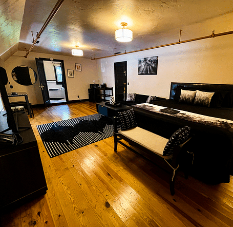 corner view of a room featuring a double bed along with a common seating are in the far end highlighting the black furnishings and decor - Historic Tapoco Lodge