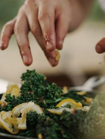 Hands seasoning a green leafy salad with slices of lemon in a blurred kitchen setting - BluSalzz Collection - Tranquil Resort, Wayanad