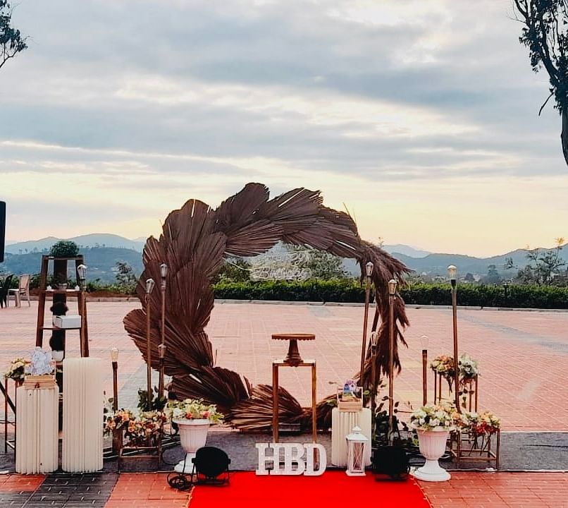 An outdoor wedding venue is set up with a floral arch and red carpet, with a scenic view in the background | Open Deck | Woodstock Resorts, Coorg