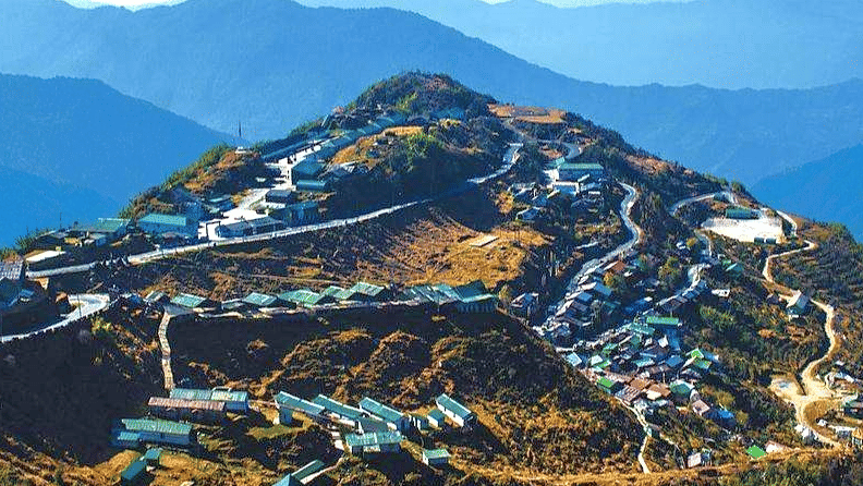 Aerial view of Zuluk village nestled among the Himalayan hills in East Sikkim, with winding roads and layered blue mountain ranges in the background.