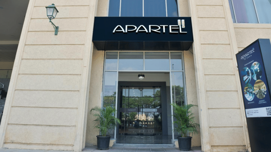A close-up of a classical stone building facade featuring an arched entrance, a black sign, and a traditional green wall lantern at Apartel by Aarin, Oragadam.