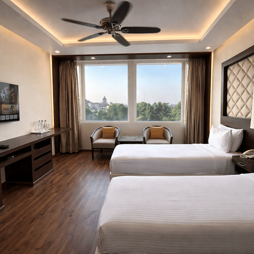 A Superior Room Twin bed at Clarks Avadh, Lucknow, featuring twin beds, spreads, pillows, a television, and large windows.