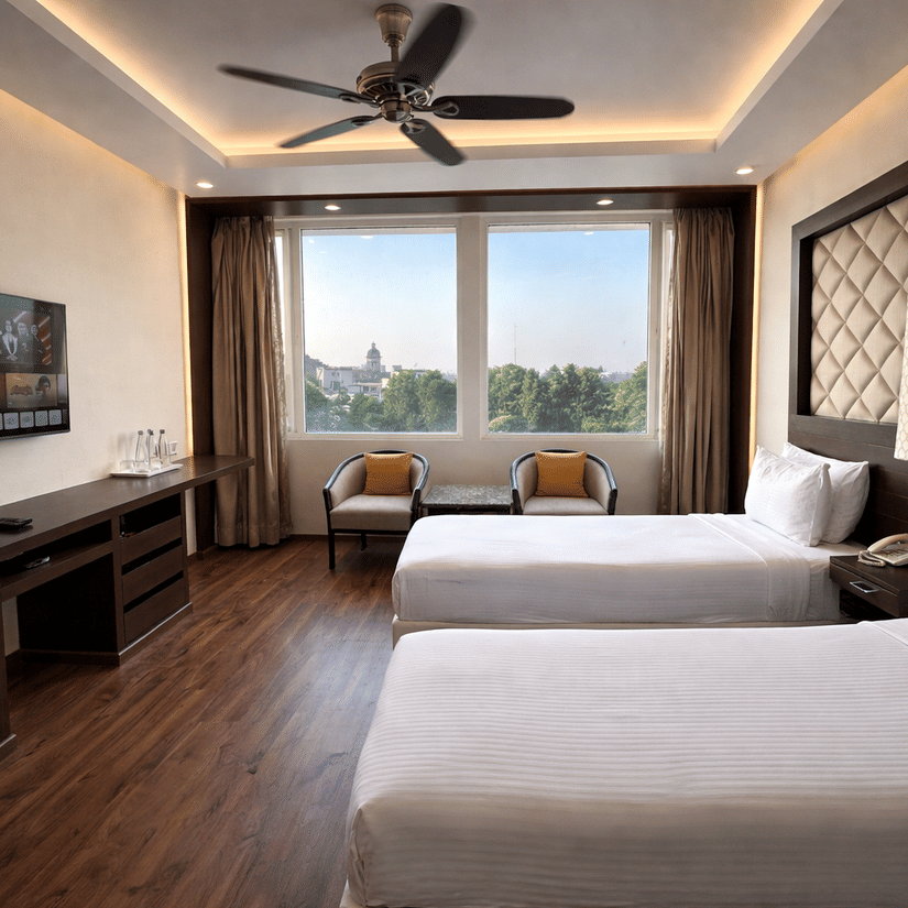 A Superior Room Twin bed at Clarks Avadh, Lucknow, featuring twin beds, spreads, pillows, a television, and large windows.