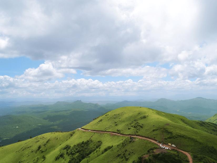 An aerial view of lush green hills with cloudy sky in the background.