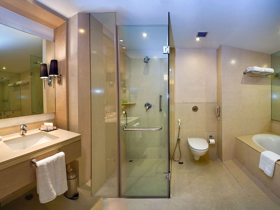 Interior view of a bathroom featuring a glass shower, a bathtub with a towel, and a sink- The Sonnet, Kolkata.