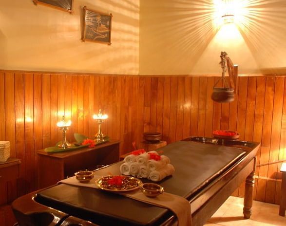 Warmly lit spa treatment room with a massage table and various wellness products - BluSalzz Collection - Tranquil Resort, Wayanad