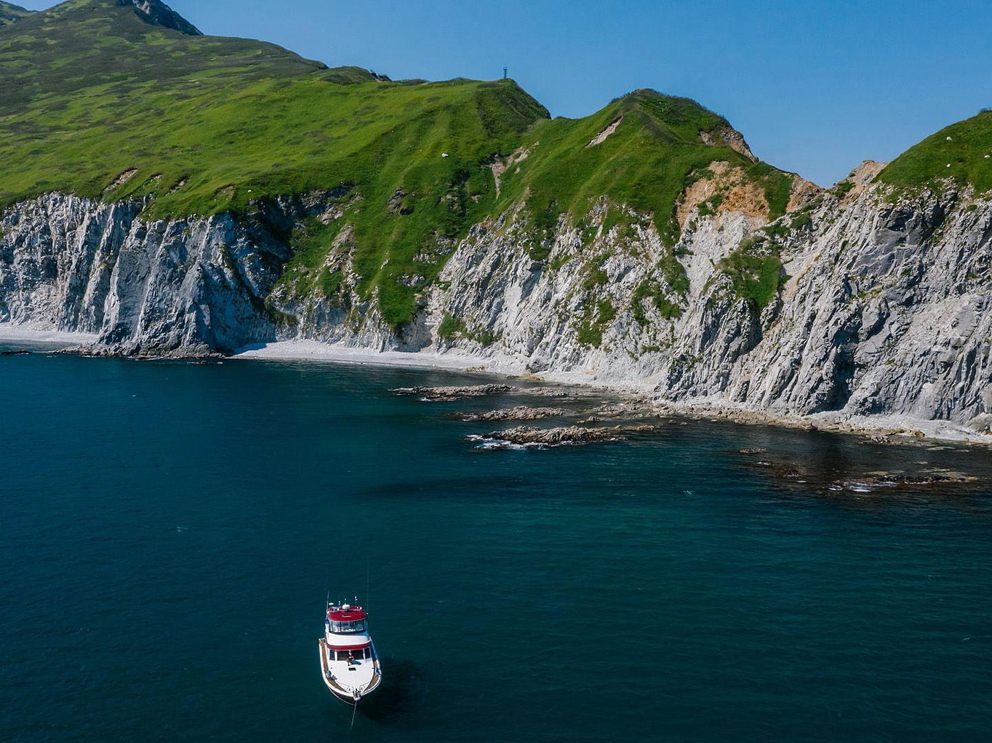 An image of a boat in a deep blue sea and green mountains in the background