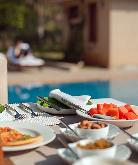 An outdoor buffet table with various dishes and a swimming pool in the background - Shreyas Retreat