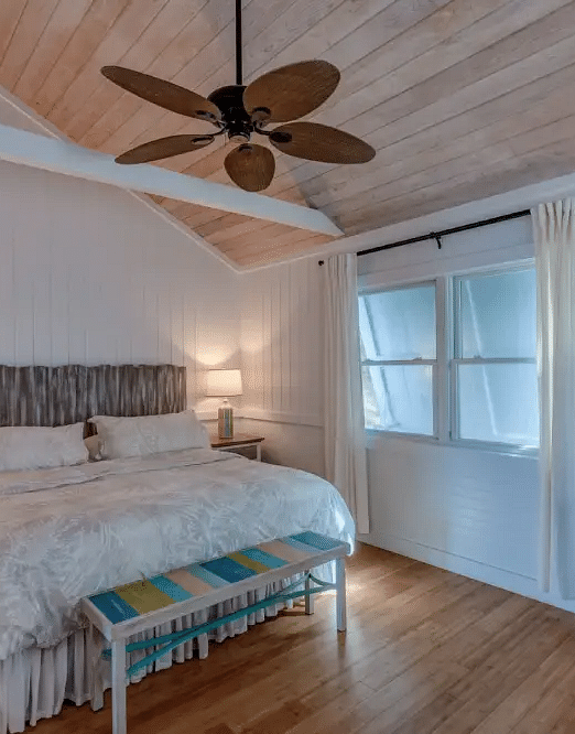 Bright bedroom with a double bed, ceiling fan, white walls, and a baby crib placed near the window in a guesthouse | Abaco Inn