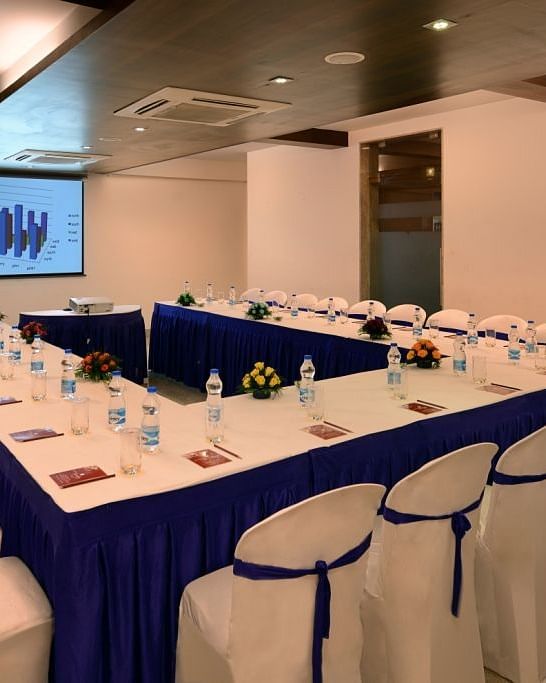 A conference room at the Dwarkadhish Lords Eco Inn set up with a U-shaped table, chairs, and a projection screen.