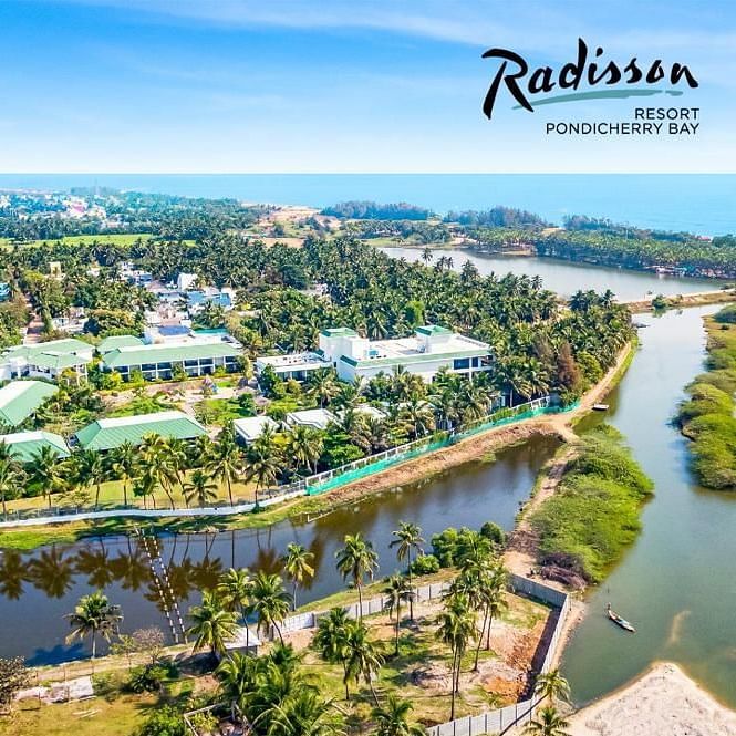 Aerial view of Radisson Pondicherry Bay with lush greenery, a lagoon, and the sea in the background.