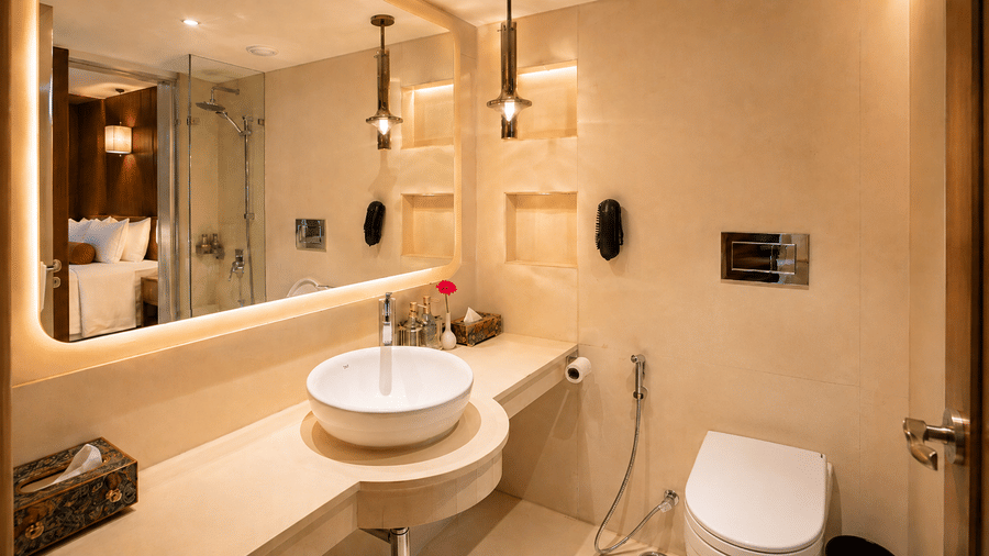 Modern bathroom at Pride Premier Pune with a round basin, mirror, toilet and warm ambient lighting.