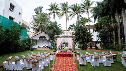 A lawn with chairs and a decorated stage with palm trees in the background at the best resort in Bangalore | Ramanashree California Resort