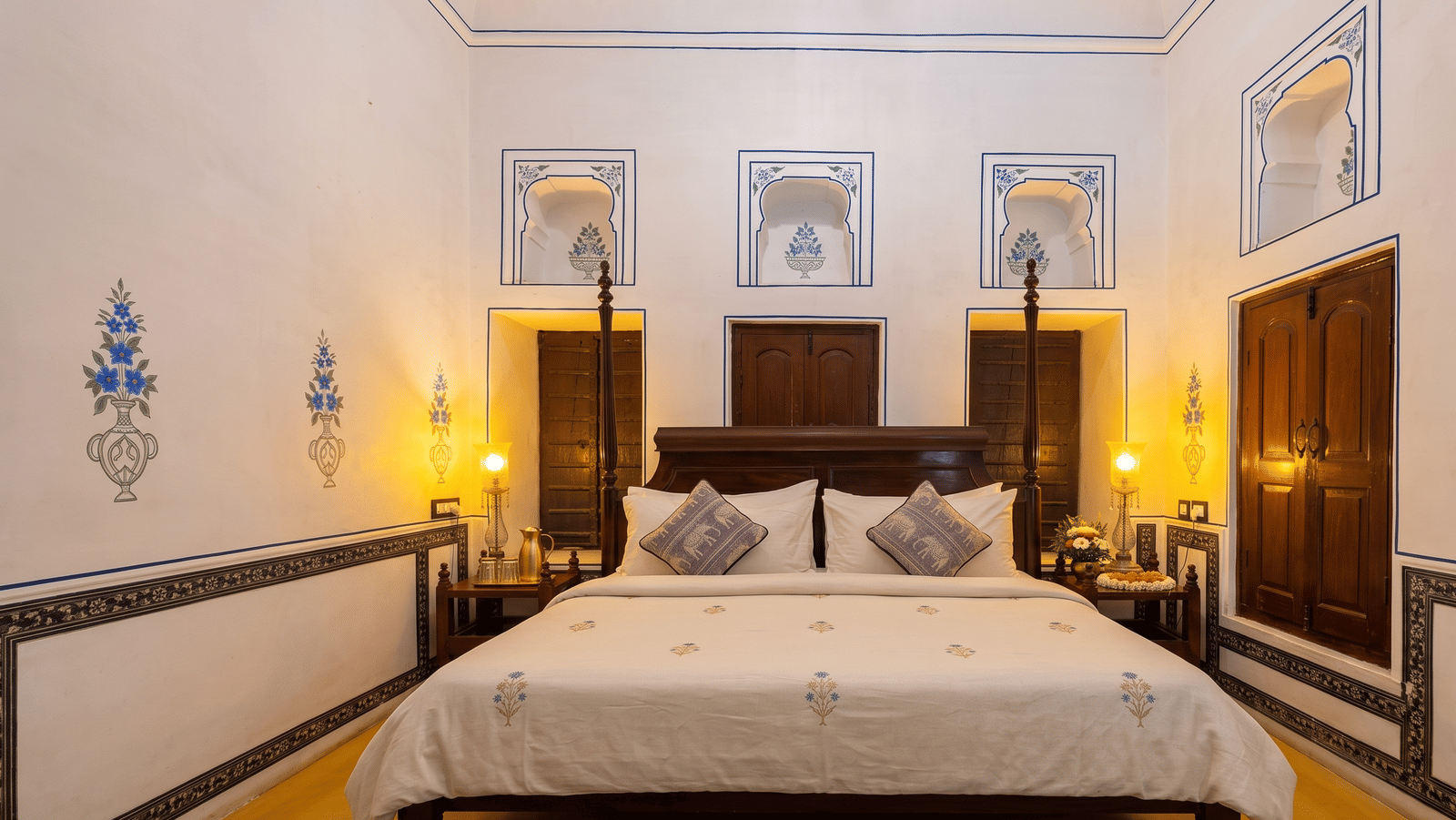 Heritage bedroom with a four-poster bed, hand-painted blue floral motifs, arched wall niches and lamp-lit bedside tables at BluSalzz Vintage - Harlalka Haveli.