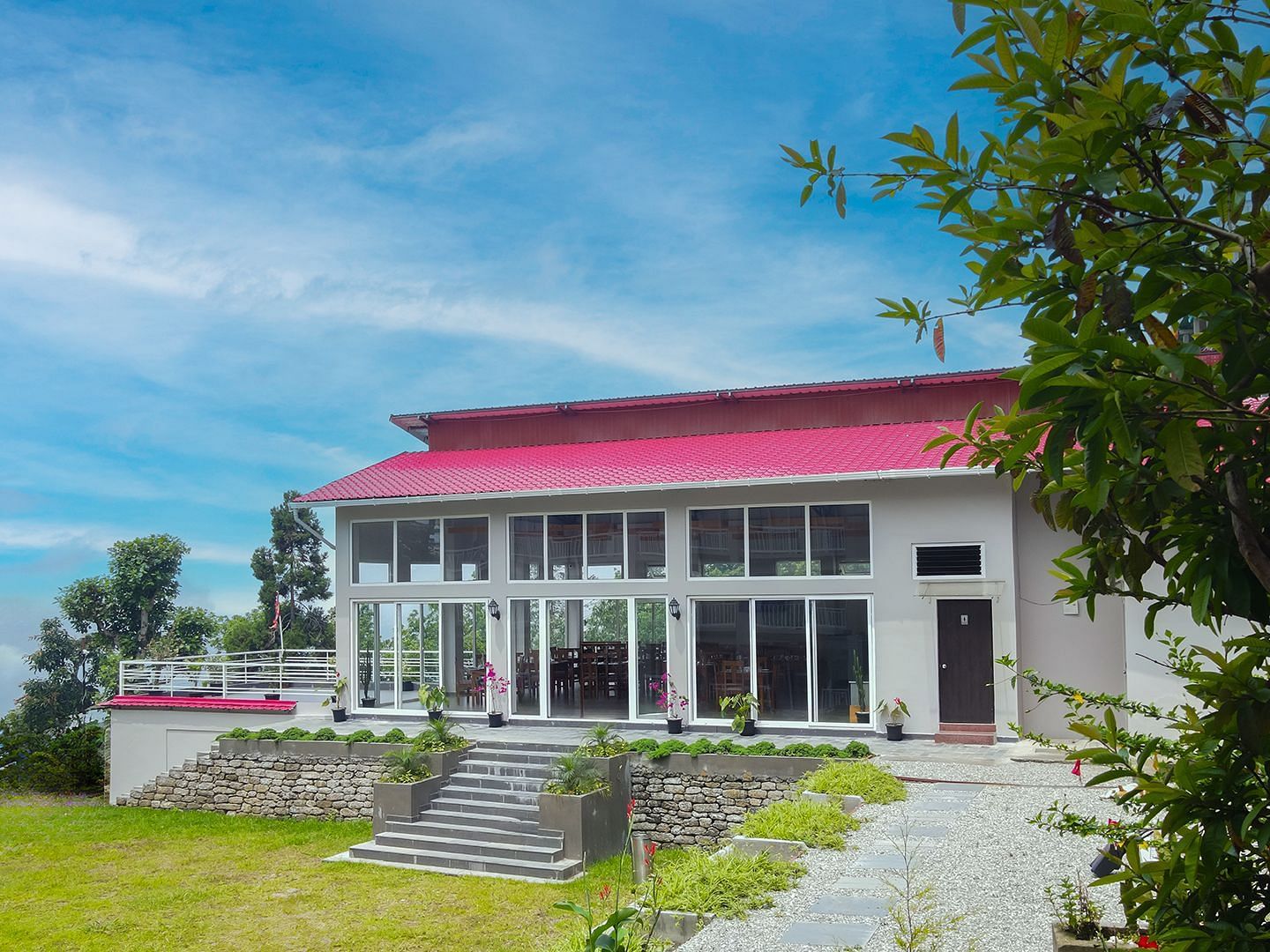 A modern hotel building at Yashshree Resorts & Spa, Kalimpong, with a distinctive red roof, set amidst lush greenery and a bright blue sky.