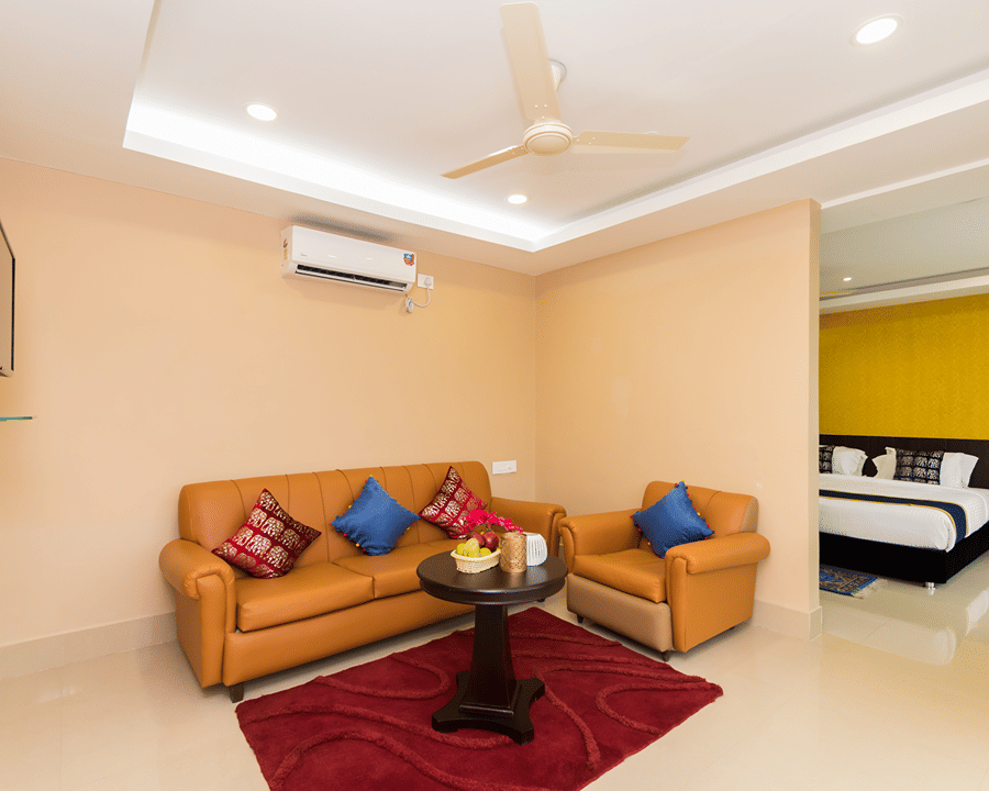Sitting room of the Suite featuring a set of 2 sofas around a coffee table with a TV on the wall opposite to the way to the bedroom at Central Courtyard Boutique Hotel, Siliguri