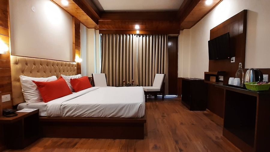 An image of a bedroom featuring a double size bed, a flat TV screen, a cabinet for storing things and a seating area at one corner - Mastiff Xanadu, Manali